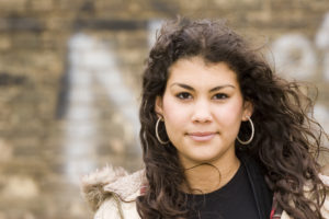 Dark haired girl with hoop earrings, outside, looking at the camera. 